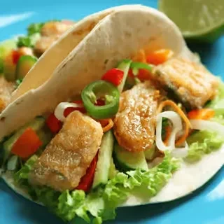 Two soft-shell tacos filled with fried fish/chicken and colorful vegetables.