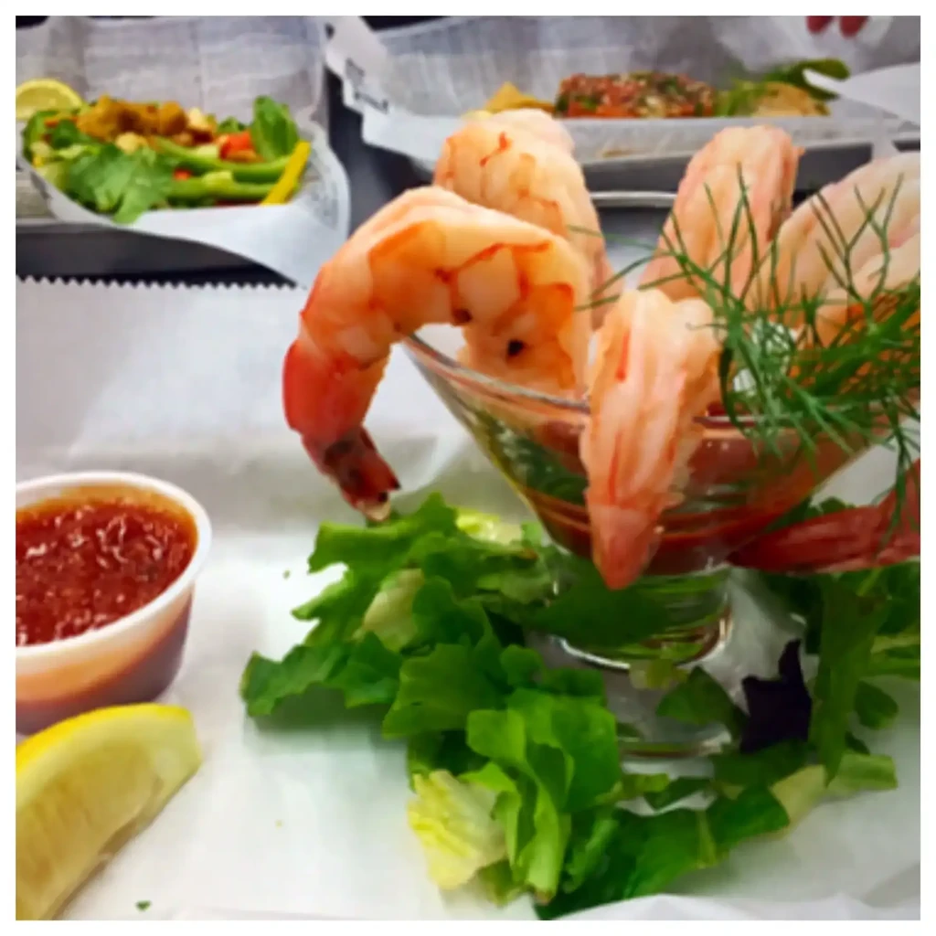 Shrimp cocktail in a glass, garnished with dill, sauce, and lemon.
