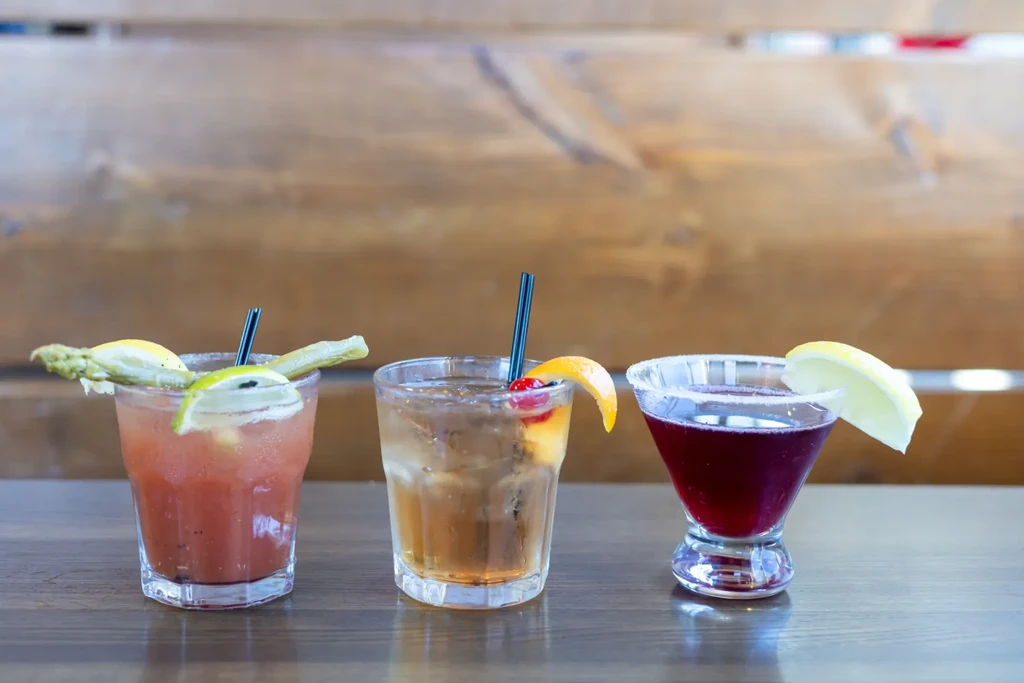Three colorful, garnished cocktails on a dark wooden surface.