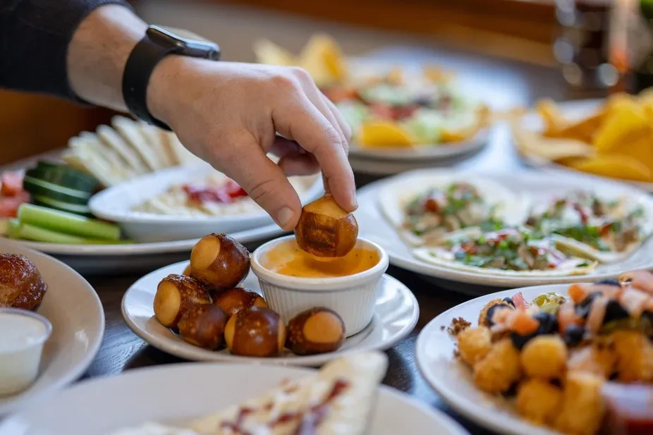Hand with smartwatch dips golden pretzel bite into creamy cheese sauce.