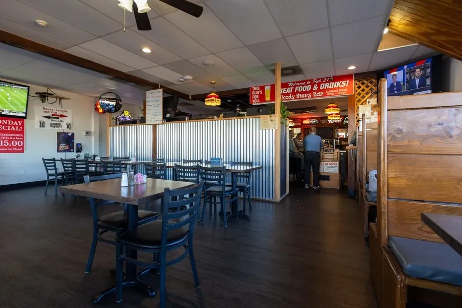 Casual restaurant interior, empty tables, sports on TV, people at bar.