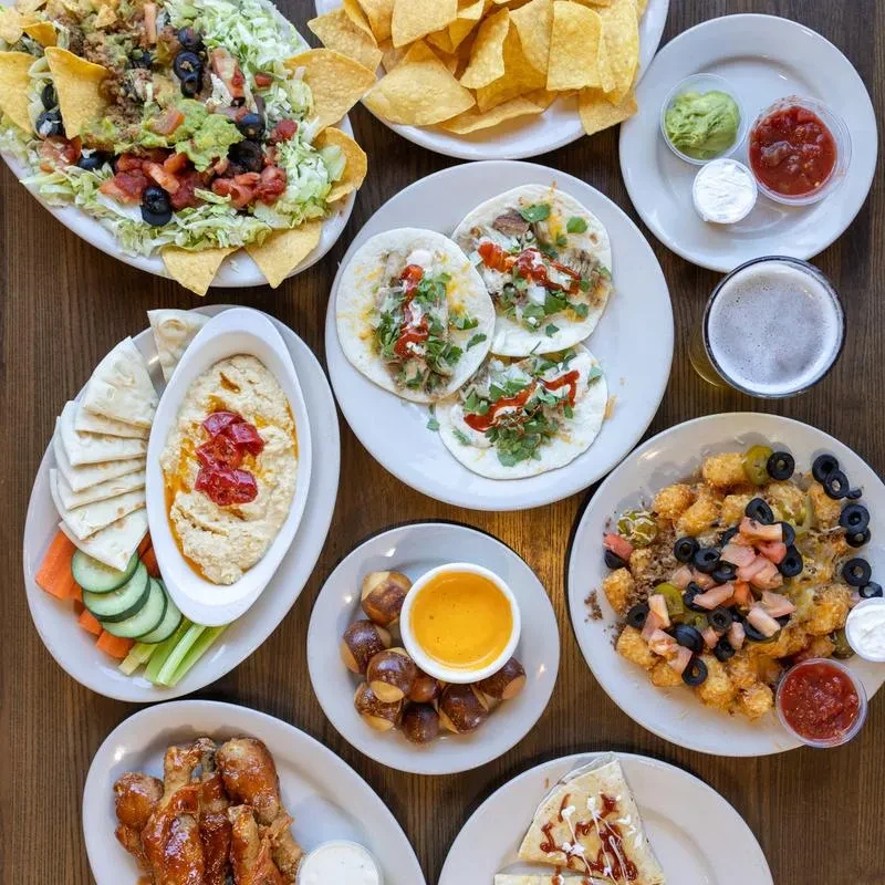 An overhead view of a wooden table with diverse appetizers and beer.