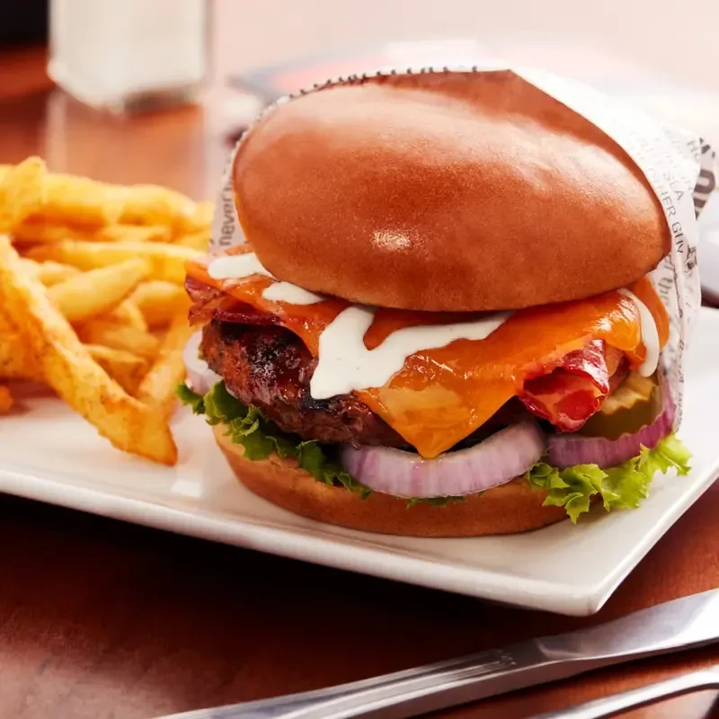 Gourmet burger with fries on a white plate on a wooden table.