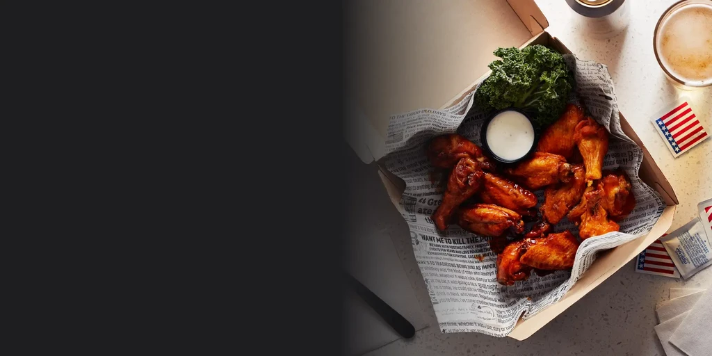 Overhead: takeout chicken wings, white sauce, beer, American flag accents.