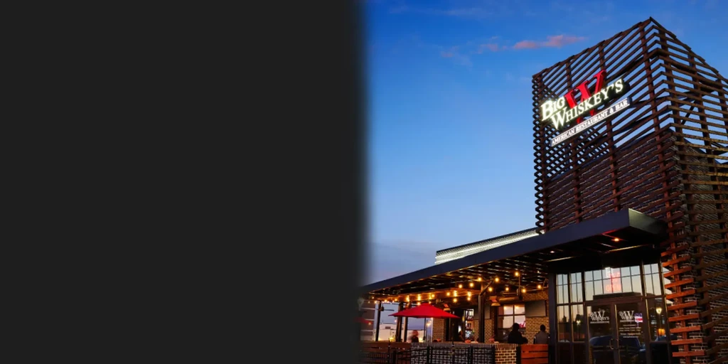 Big Whiskey's restaurant exterior: wooden lattice, illuminated sign, patio at dusk.