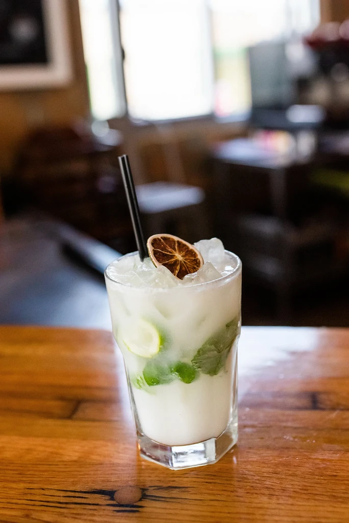 White iced drink with mint, lime, straw, in hexagonal glass.