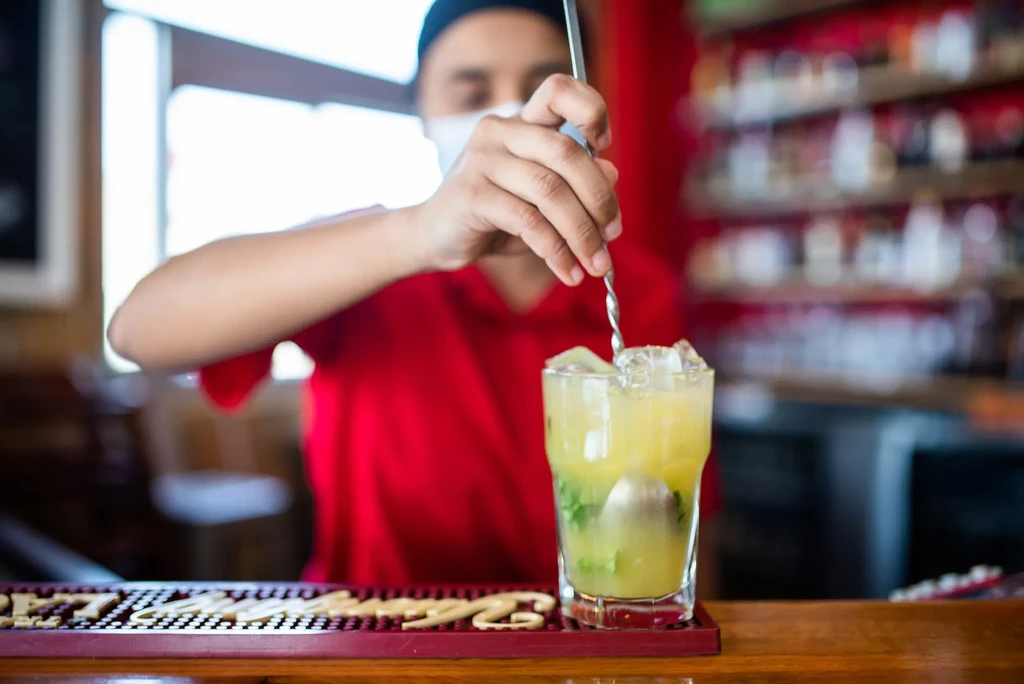 Bartender stirring a cocktail with mint, ice, and a round ice ball.
