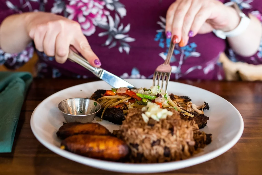Close-up of hands cutting a colorful meal of protein, rice, plantains.