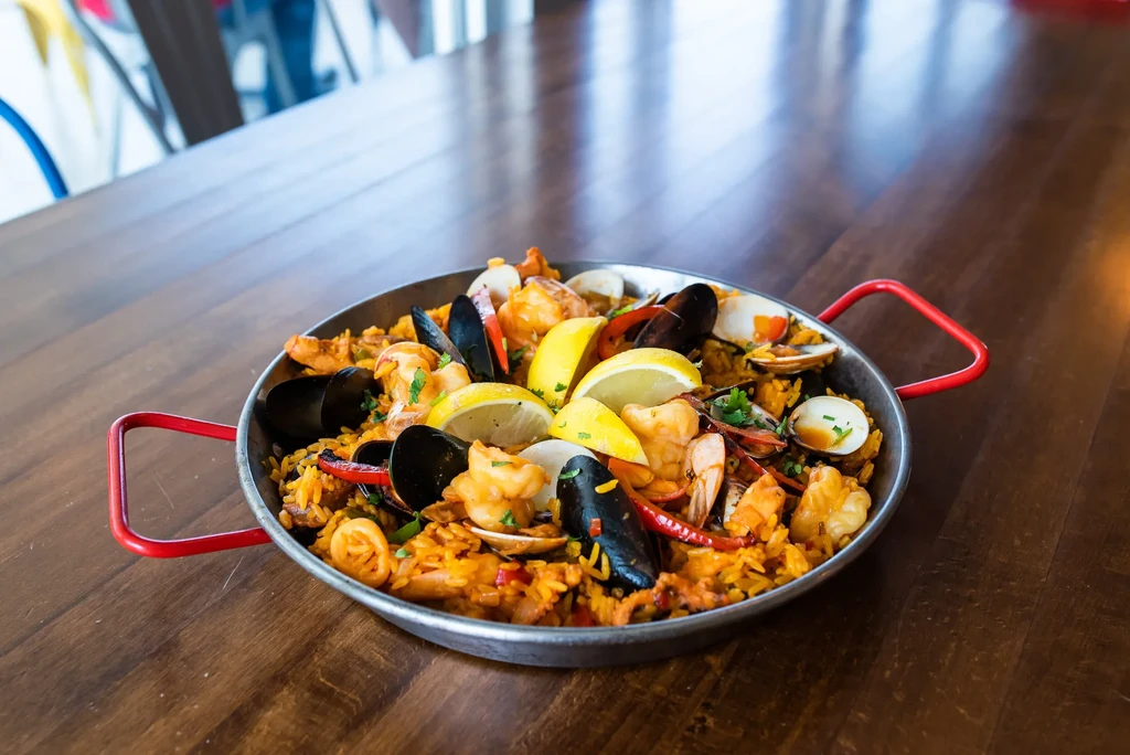 Seafood paella in a rustic pan, garnished with lemon and parsley.