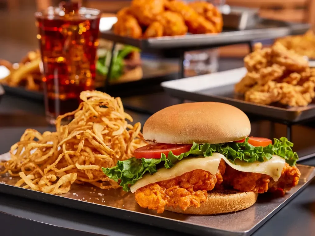 Fried chicken sandwich with onion straws and a dark iced drink.