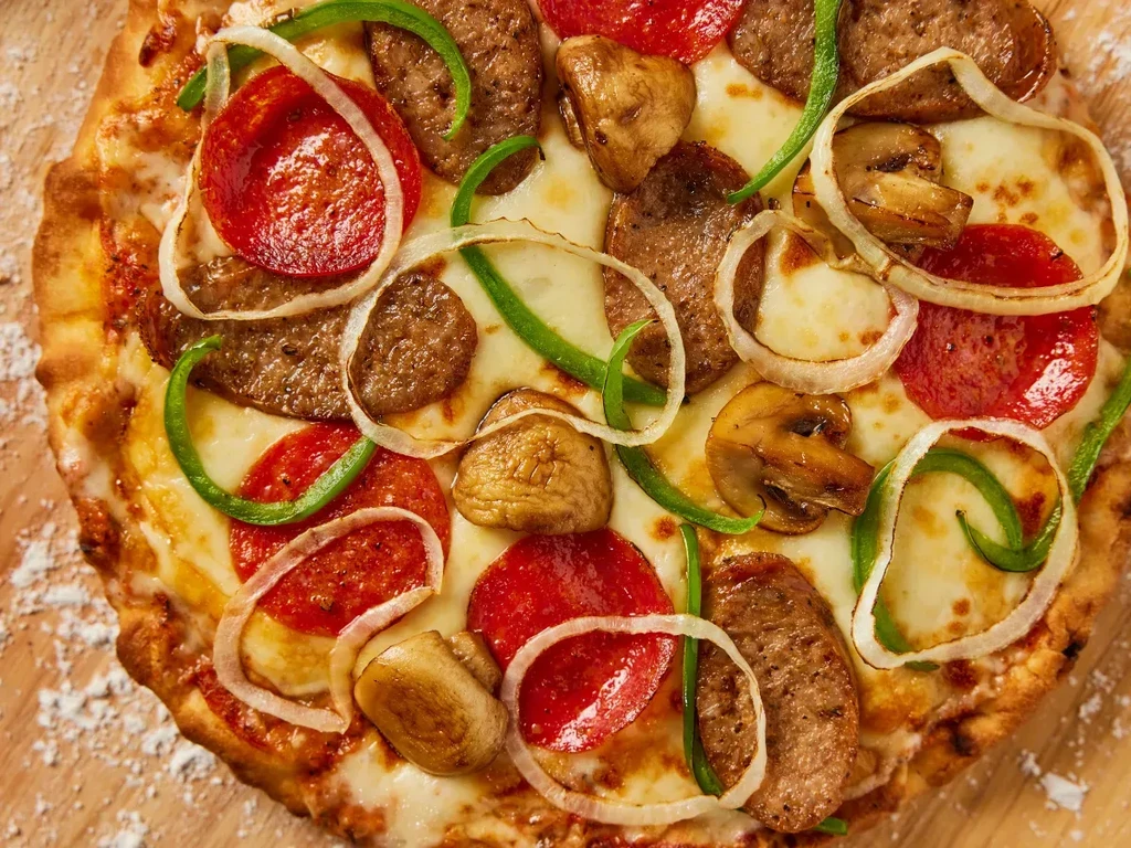Close-up of a baked pizza with pepperoni, sausage, mushrooms, and vegetables.