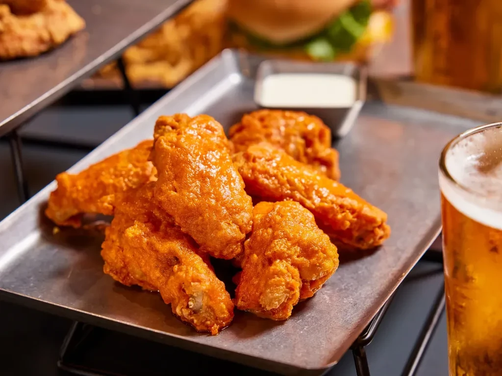 Crispy buffalo chicken wings on a tray with dipping sauce and beer.