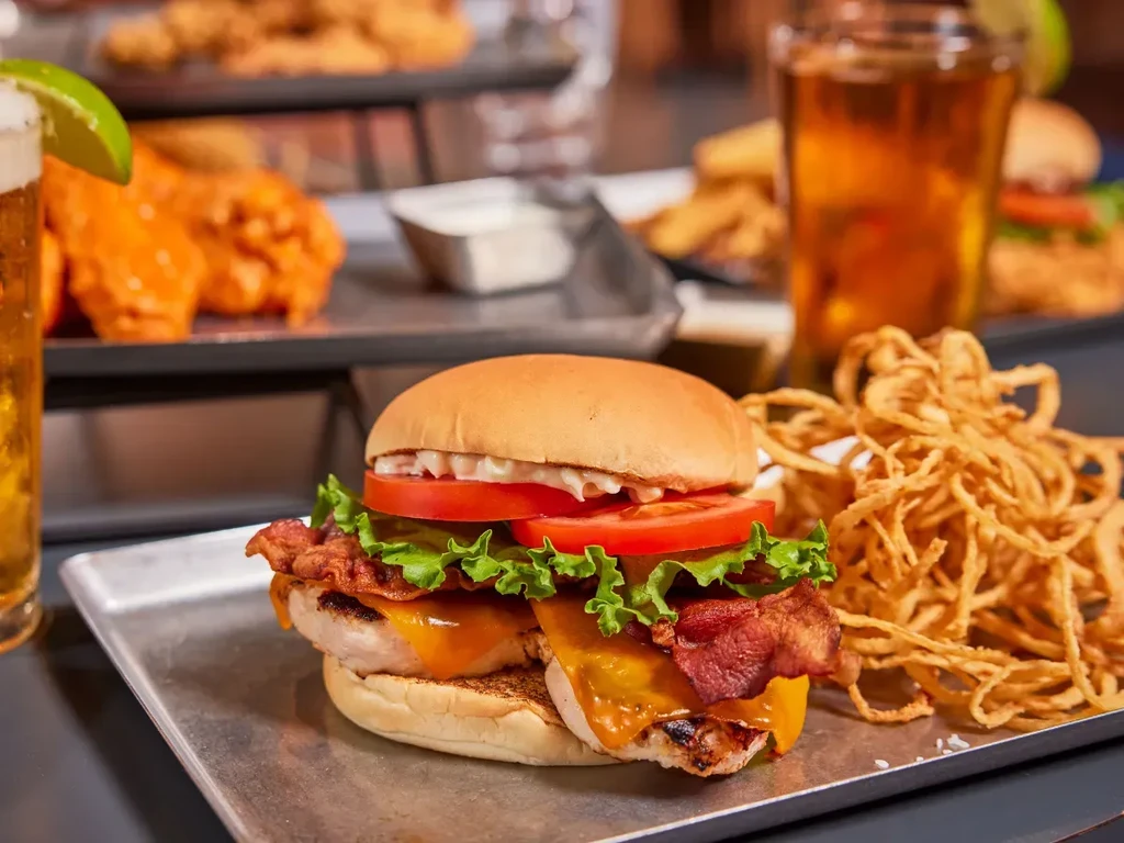 Close-up of chicken sandwich with bacon, cheese, onion strings, and beer.