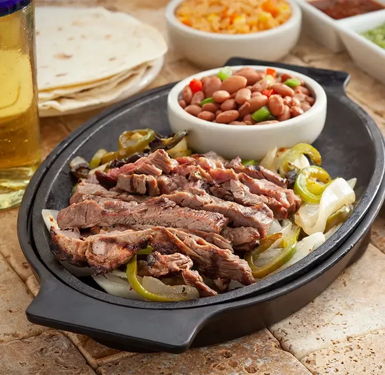 Sizzling steak fajitas skillet, pinto beans, Spanish rice, tortillas, sauces.