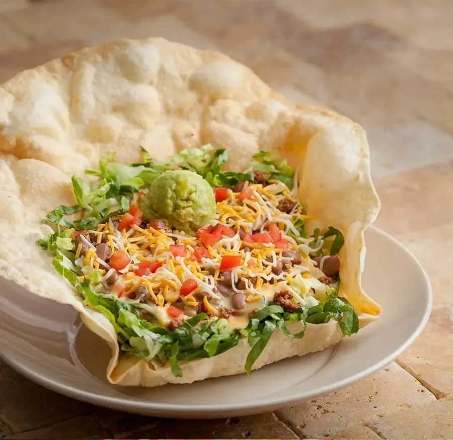 Taco salad in a crispy tortilla bowl with meat, cheese, tomatoes, guacamole.