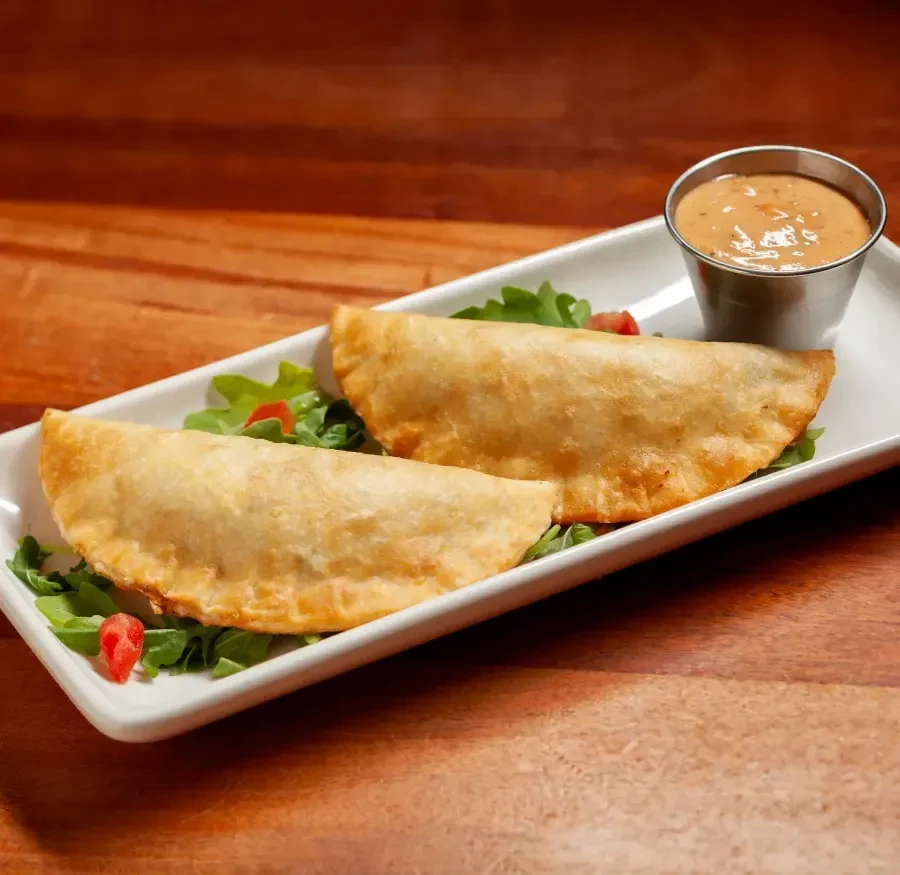 Two golden-brown crescent pastries with greens and dipping sauce.