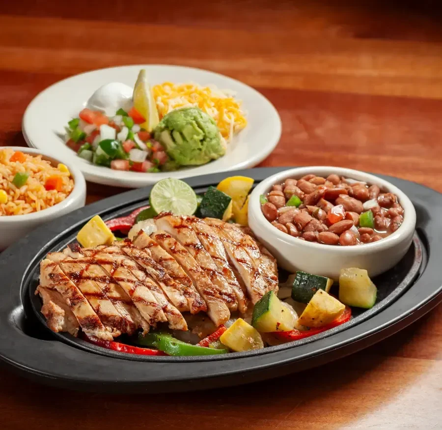 Grilled chicken fajitas with beans, rice, guacamole, and toppings.