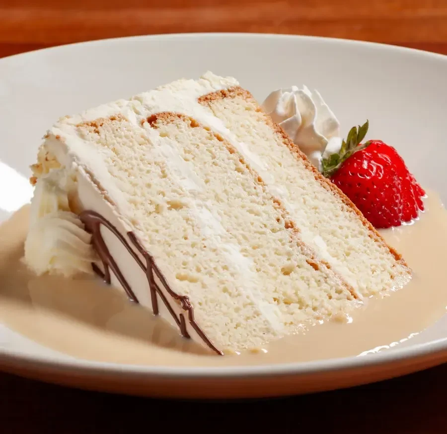 Layered white cake with chocolate drizzle, whipped cream, strawberry, and sauce.