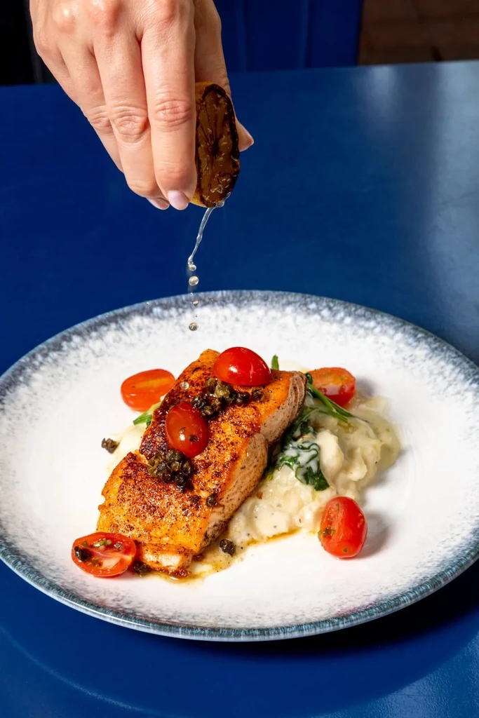 Pan-seared salmon, mashed potatoes, and hand squeezing charred lemon over meal.