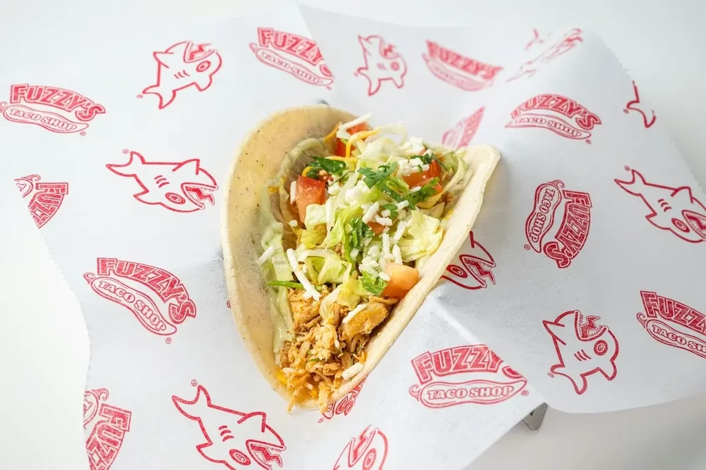 A single soft-shell chicken taco on Fuzzy's Taco Shop branded paper.