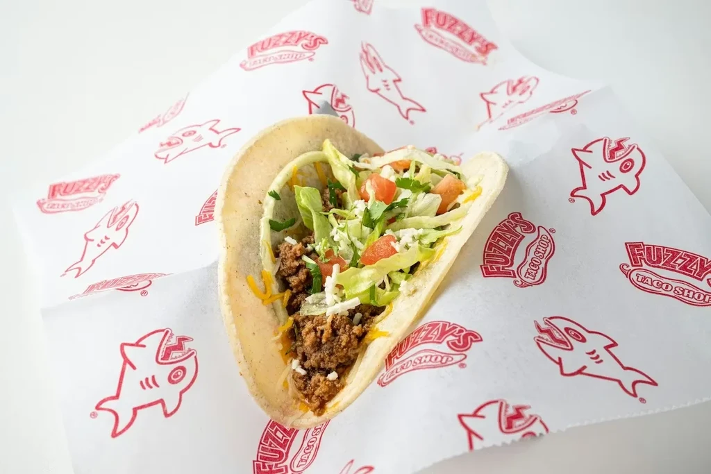 Soft taco with ground meat, lettuce, tomato, cheese on Fuzzy's wrapper.