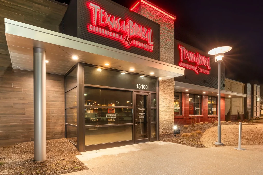 Modern Texas de Brazil steakhouse exterior at night, red neon sign glowing.
