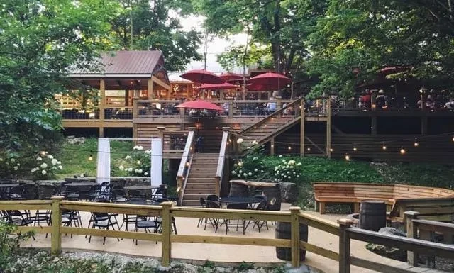 Multi-level wooden outdoor restaurant with red umbrellas surrounded by trees.