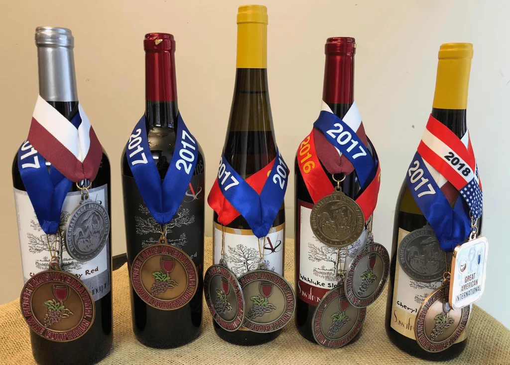Five wine bottles in a row, displaying numerous award medals and ribbons.