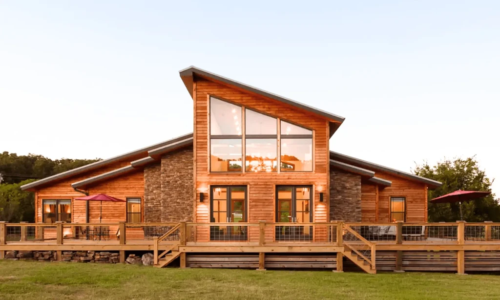 Modern-rustic lodge with wood, stone, large deck, red umbrellas, lawn.