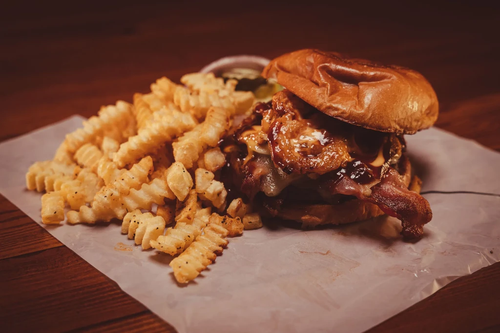 Gourmet burger with bacon, cheese, and crinkle fries on dark wood.