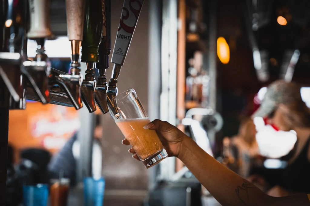 A hand fills a glass with Coors Light beer from a tap.