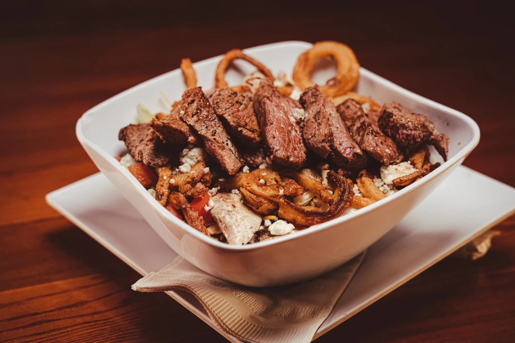 Grilled steak bowl with crispy onion rings, cheese, and vegetables.