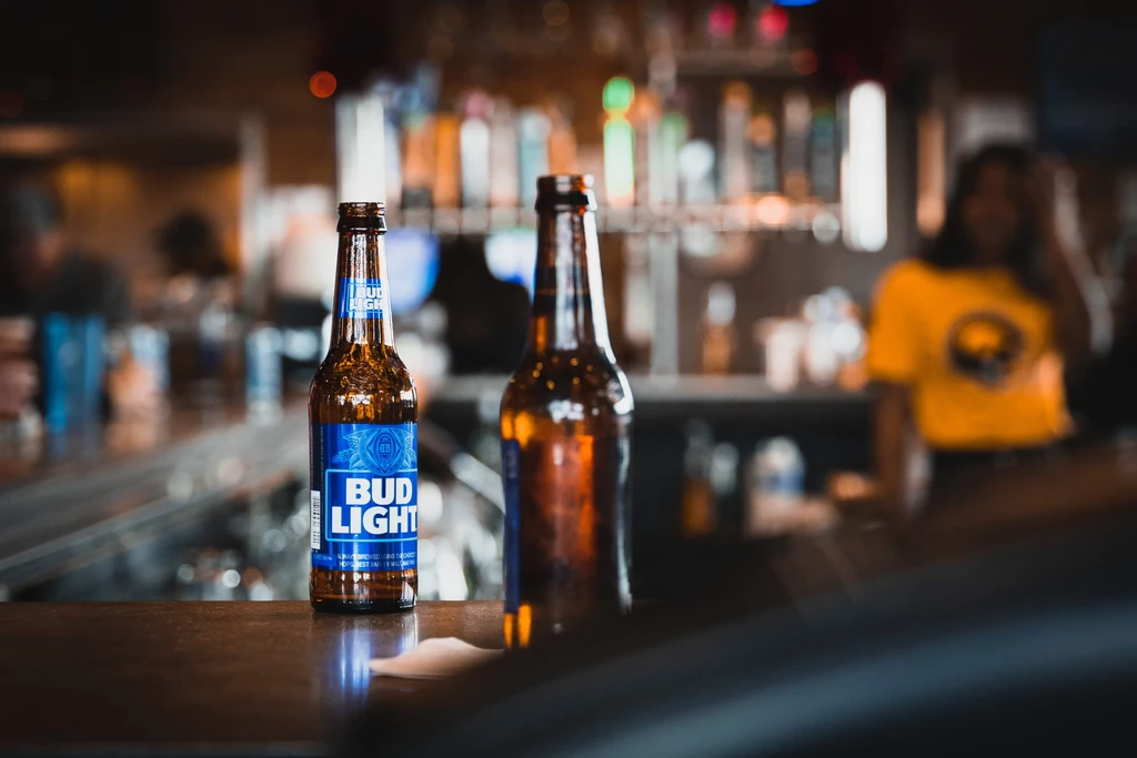 A Bud Light and brown beer bottle on a bar counter.