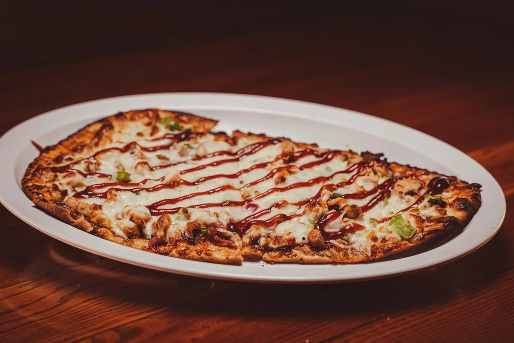 Oval flatbread pizza with chicken, cheese, greens, and barbecue sauce.