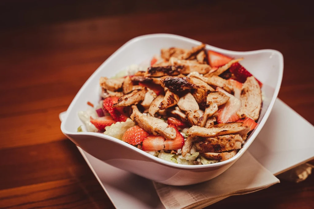 Grilled chicken and strawberry salad in a modern white bowl.