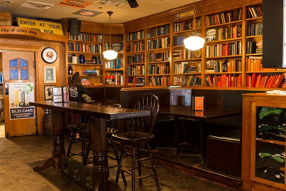 Warmly lit bar with extensive dark wood bookshelves and various seating.