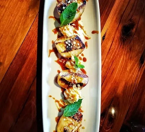 Plated grilled fruit, cream, nuts, mint, and caramel on wood.