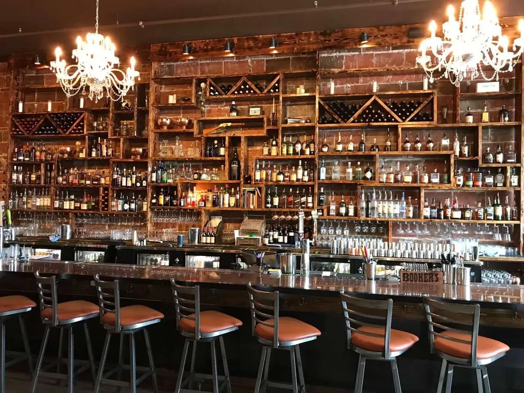 Bar with floor-to-ceiling liquor shelves on rustic brick wall, bar stools.