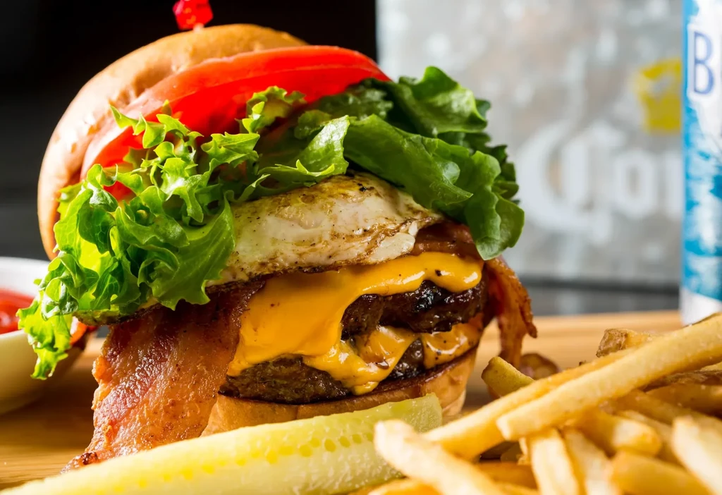 Stacked burger with bacon, fried egg, fries, and pickle.