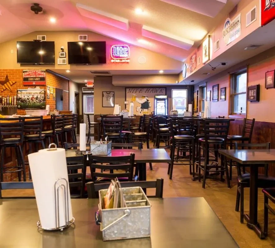 Empty sports bar with tables, bar, multiple TVs, and sports decor.