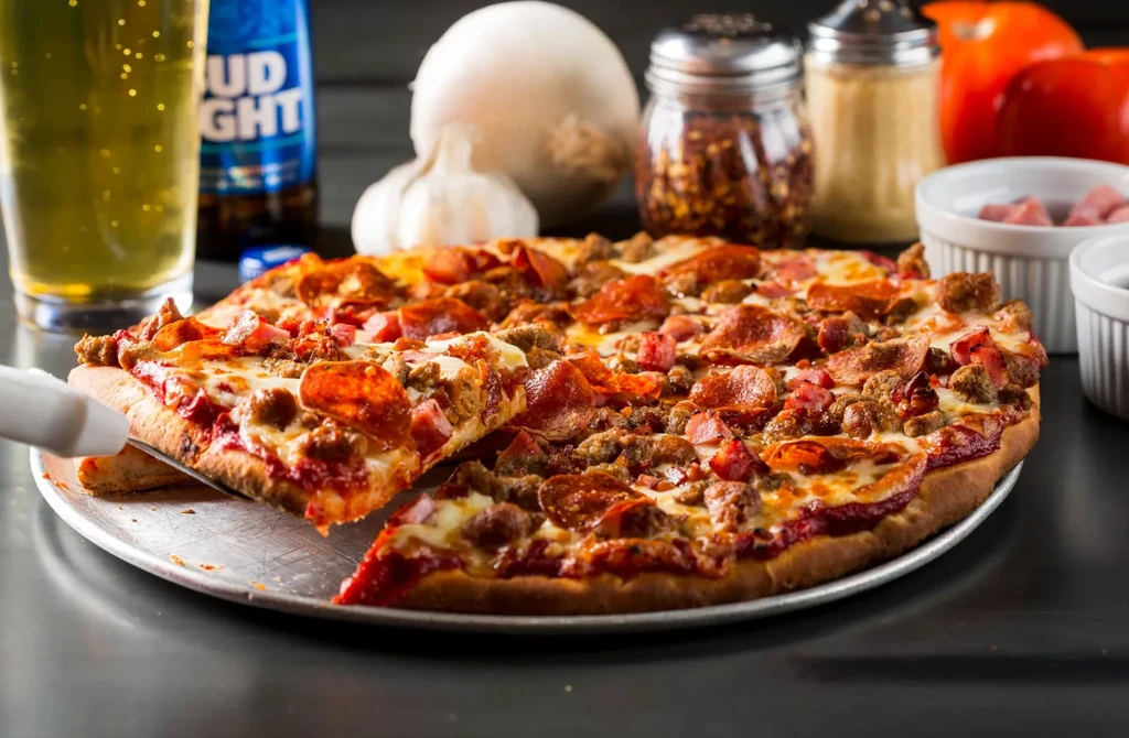 Meat lover's pizza with slice being lifted, beer, and fresh ingredients.