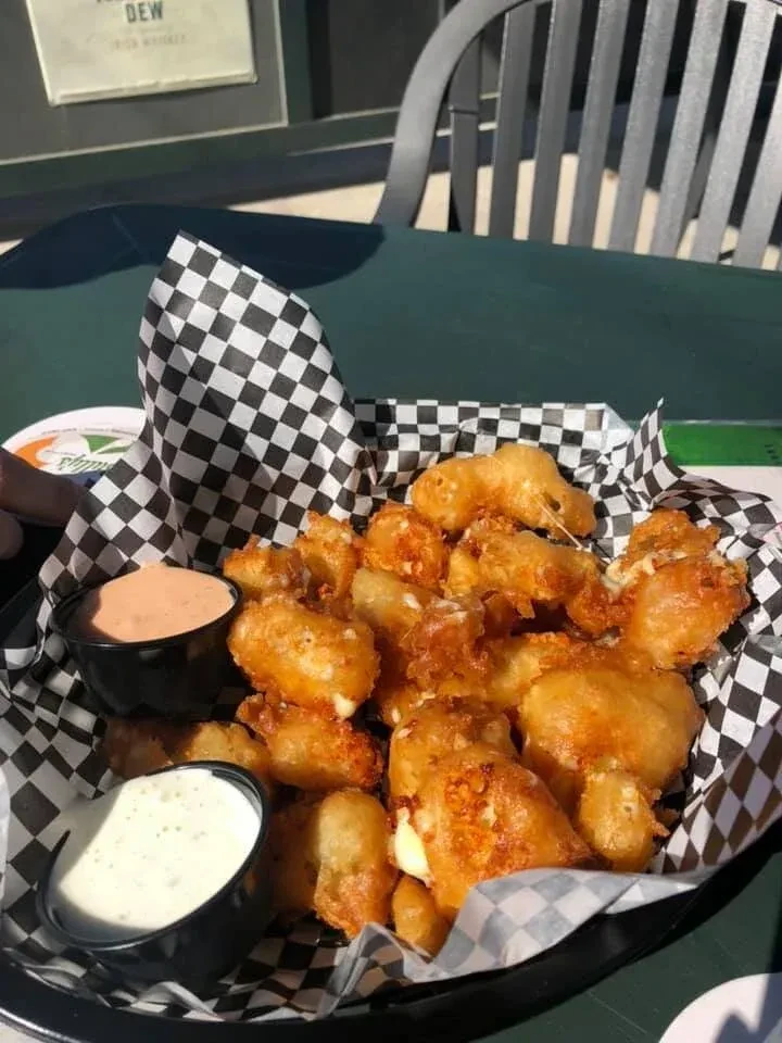 Black basket of golden-brown fried cheese curds and two sauces.