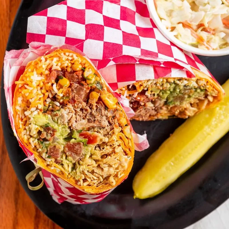 Burrito cut in half showing fillings, with a pickle and coleslaw.