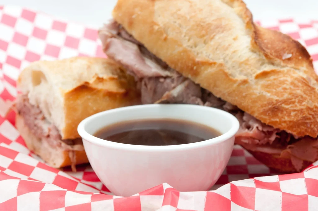 French dip roast beef sandwich with au jus on checkered paper.