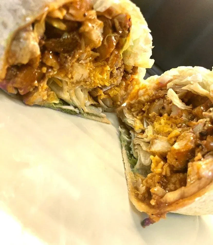 Half a burrito, filled with meat, cheese sauce, and green lettuce.