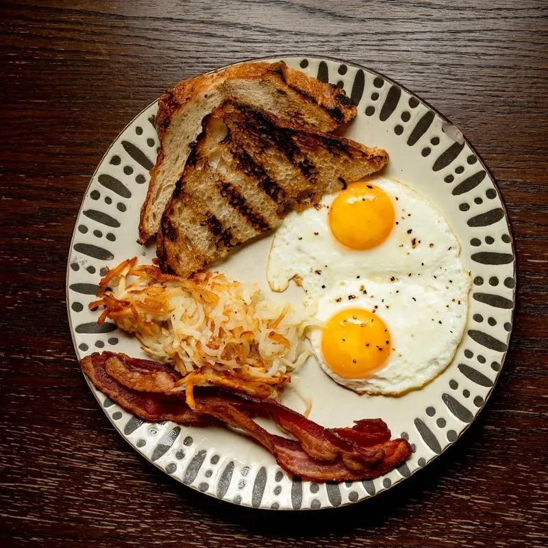 Fried eggs, bacon, hash browns, and toast on a patterned plate.
