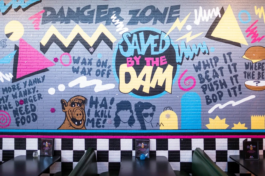 Colorful 80s/90s pop culture mural in a retro restaurant with green booths.