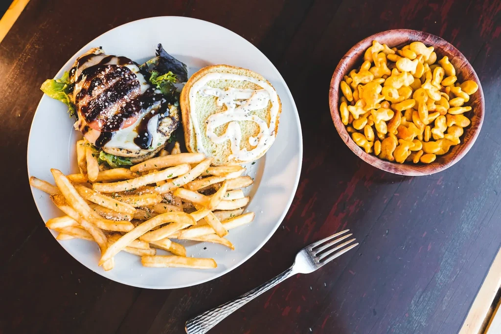 Overhead view: Burger, fries, Goldfish crackers, and a fork on wooden table.