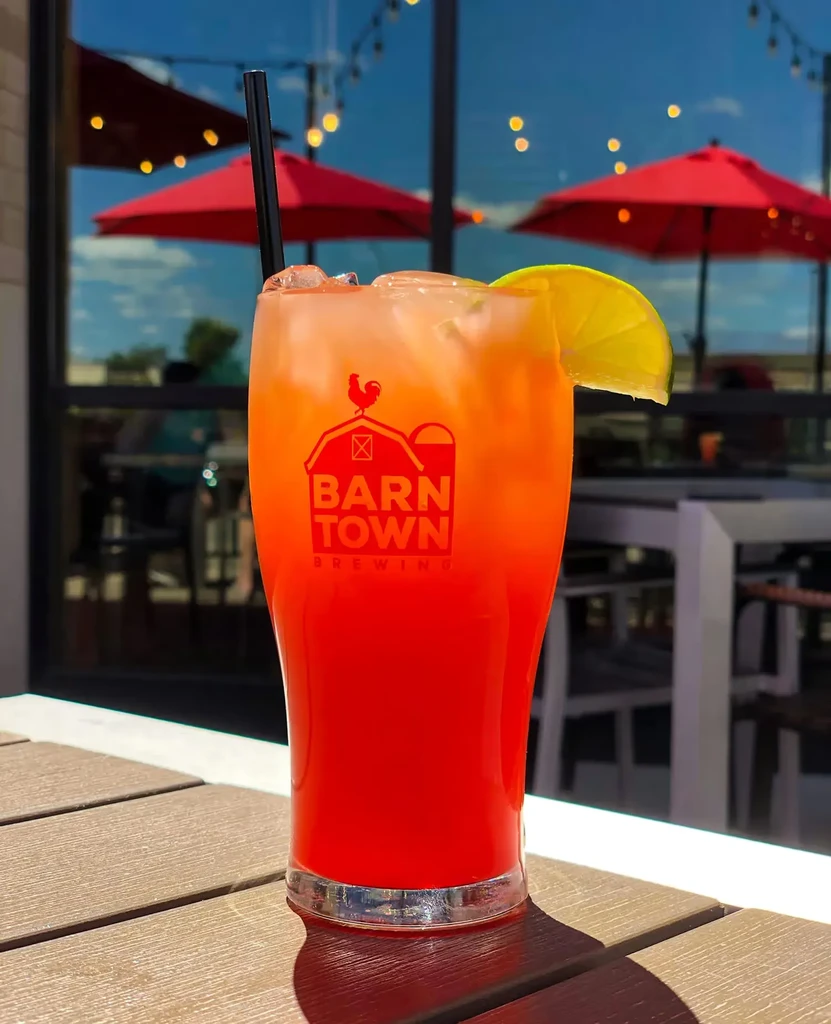 Layered orange and red drink with lime on an outdoor table.