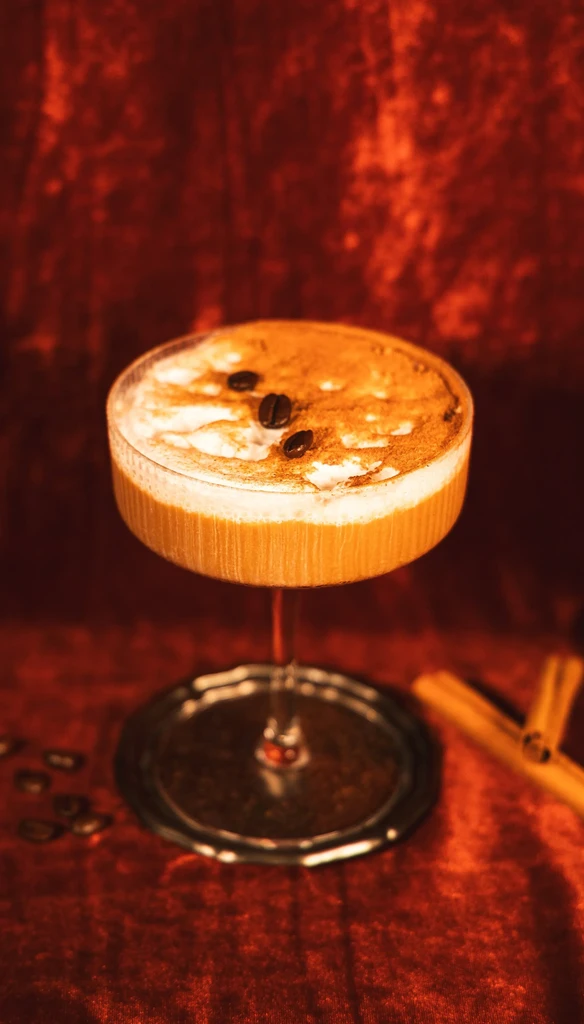 Layered cocktail with frothy foam, coffee beans, and cinnamon dusting.